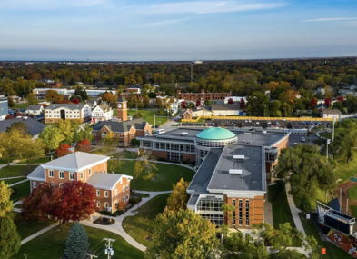 Aerial view of a vibrant college campus with modern and traditional architecture, surrounded by lush greenery and autumn colors.