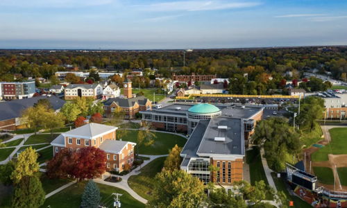 Aerial view of a vibrant college campus with modern and traditional architecture, surrounded by lush greenery and autumn colors.