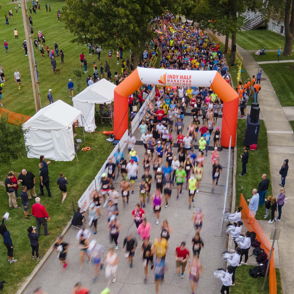 Lively running event with colorful participants racing through an orange and white archway, showcasing community spirit and excitement.