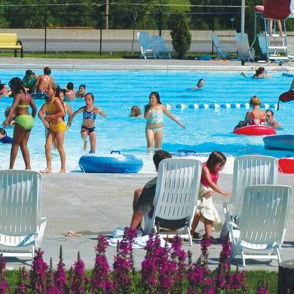A lively pool scene with people playing, relaxing, and enjoying a sunny day among colorful inflatables and flowers.