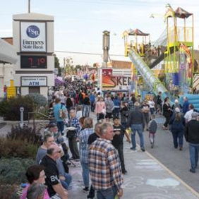 A vibrant fair scene with diverse crowds enjoying colorful tents, rides, and a joyful atmosphere of celebration.