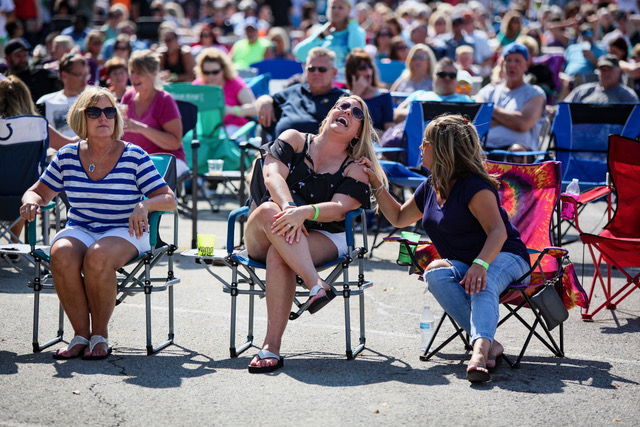 A joyful outdoor event with a large crowd, three women laughing together, creating a relaxed and festive atmosphere.