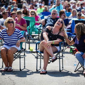 A joyful outdoor event with a large crowd, three women laughing together, creating a relaxed and festive atmosphere.