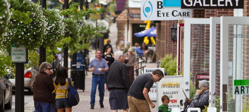 Busy urban street scene with diverse people, shops, greenery, and cheerful decorations, evoking community and connection.
