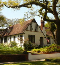 Charming traditional home with gabled roof, surrounded by lush gardens and a large tree, evoking warmth and nostalgia.