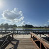 Serene lakeside scene with a wooden dock, calm water, bright blue sky, and fluffy clouds, evoking tranquility and relaxation.