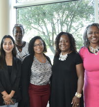 Six diverse women stand together indoors, exuding camaraderie, positivity, and a warm sense of community and empowerment.