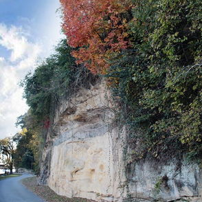 Scenic cliffside landscape with autumn colors, dynamic clouds, a tranquil pathway, and serene water, evoking peace and beauty.