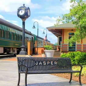 A serene railway station with a green train, a "JASPER" bench, and a clock tower, evoking nostalgia and tranquility.