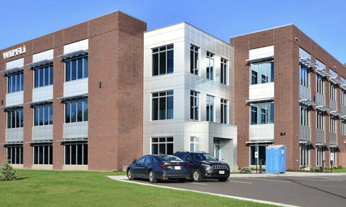 Contemporary three-story building with brick facade, large windows, and landscaped lawn; evokes professionalism and positivity.