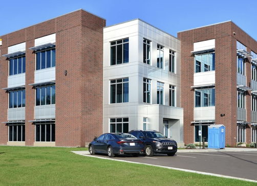 Contemporary three-story building with brick facade, large windows, and landscaped lawn; evokes professionalism and positivity.