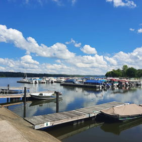 A serene marina scene with docked boats, a calm lake, bright blue sky, and fluffy clouds, evoking peace and relaxation.