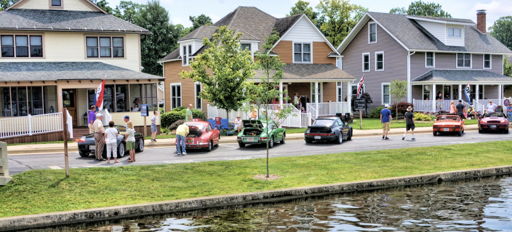 Two people kayak in calm waters by charming homes; a group onshore enjoys a sunny day, enhancing the scene's warmth and community.