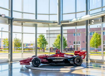 Red race car displayed in a bright glass space, surrounded by greenery, evoking excitement and admiration for automotive engineering.