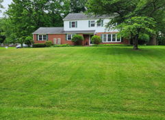 A serene single-family home with large windows on a lush lawn, surrounded by trees, evokes comfort and a connection to nature.