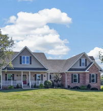 Charming house with brick and siding, lush yard, tall trees, and bright sky evoke comfort, happiness, and tranquility.