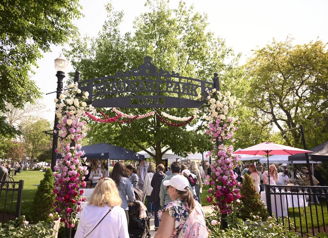 Vibrant park entrance with flowers, greenery, and people suggests a festive atmosphere, evoking joy and community spirit.