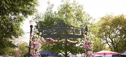Vibrant park entrance with flowers, greenery, and people suggests a festive atmosphere, evoking joy and community spirit.