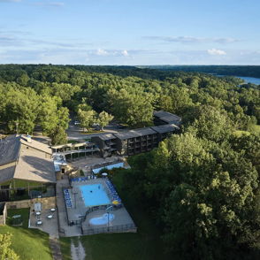 Scenic resort view with a pool, lush greenery, trees, and a lake, evoking tranquility and relaxation in a cheerful atmosphere.