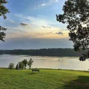 A tranquil waterfront scene with a calm lake, trees, grassy areas, and a bench, evoking peace and relaxation.