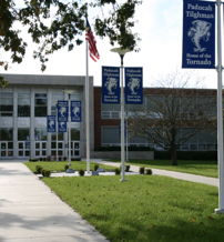 Modern Paducah High School with vibrant lawn, welcoming entrance, and flags, evoking pride and community spirit on a sunny day.