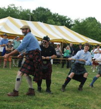 Men in kilts engage in a tug-of-war at a lively outdoor festival, showcasing strength, teamwork, and community spirit.