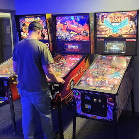 A person plays a colorful pinball machine in a dimly lit arcade, evoking nostalgia and excitement of classic gaming.