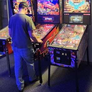 A person plays a colorful pinball machine in a dimly lit arcade, evoking nostalgia and excitement of classic gaming.