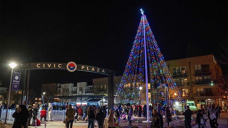 Vibrant night at Civic Plaza with a large, illuminated Christmas tree, joyful crowds, and festive, warm atmosphere.