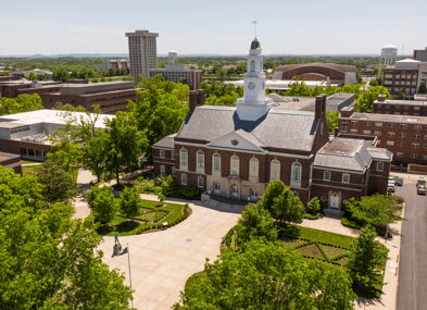 Aerial view of a university campus, featuring a steeple, lush greenery, and a blend of modern and traditional buildings.