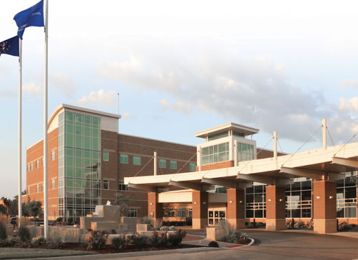 Modern healthcare facility with large glass windows, welcoming entrance, flags, evoking professionalism, safety, and hope.
