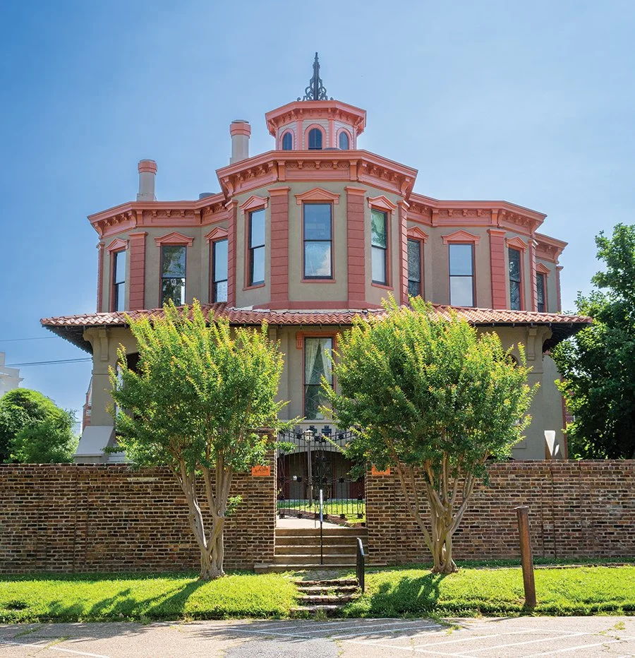 A grand reddish mansion with ornate details, surrounded by lush lawns and a stone wall, evokes nostalgia and tranquility.