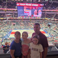 A happy family stands together in a lively sports arena, enjoying a basketball game with vibrant colors and excitement.