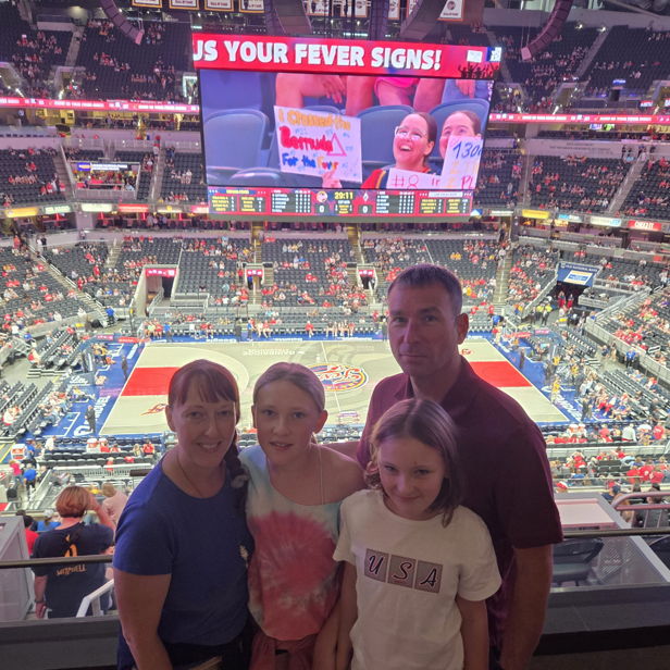 A happy family stands together in a lively sports arena, enjoying a basketball game with vibrant colors and excitement.
