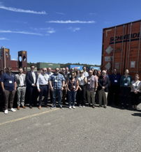 Group photo outdoors in a shipping setting, showing camaraderie, achievement, hope, and professionalism among smiling individuals.