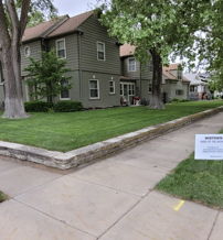 Residential area with a green lawn, trees, and a two-story house, conveying calmness and a peaceful neighborhood vibe.