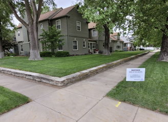 Residential area with a green lawn, trees, and a two-story house, conveying calmness and a peaceful neighborhood vibe.