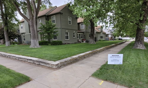 Residential area with a green lawn, trees, and a two-story house, conveying calmness and a peaceful neighborhood vibe.