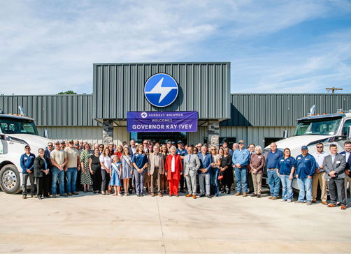 A large, diverse crowd gathers for a celebration with trucks and a banner for "Governor Ken Yeet," conveying unity and optimism.