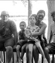 Five individuals sit casually on a railing by water, evoking joy, nostalgia, and a sense of calm camaraderie.