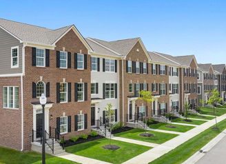 Modern townhouses with mixed brick and siding, dark shutters, neat lawns, and a clear blue sky evoke comfort and community.