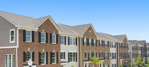 Modern townhouses with mixed brick and siding, dark shutters, neat lawns, and a clear blue sky evoke comfort and community.