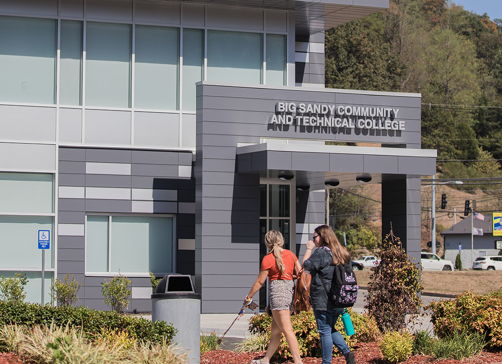 Modern educational building with large windows, brick facade, active community, and well-maintained landscaping on a sunny day.