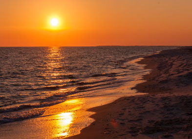 Serene sunset over the ocean with warm hues, gentle waves, and distant figures evoking tranquility and nature's beauty.
