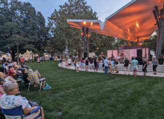 A joyful outdoor concert in a park, with performers on stage and a diverse audience enjoying a festive atmosphere.