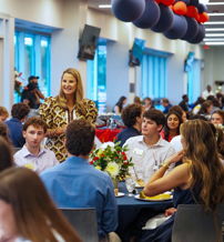 Lively gathering of diverse young people in semi-formal attire, enjoying a joyful, festive banquet with floral decor.