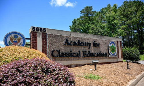 Stone sign for "Academy for Classical Education" amidst greenery and blue skies, evoking serenity and an inviting atmosphere.