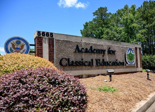Stone sign for "Academy for Classical Education" amidst greenery and blue skies, evoking serenity and an inviting atmosphere.
