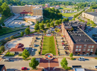 Aerial view of a vibrant town square with greenery, diverse buildings, and a central fountain, evoking community and tranquility.
