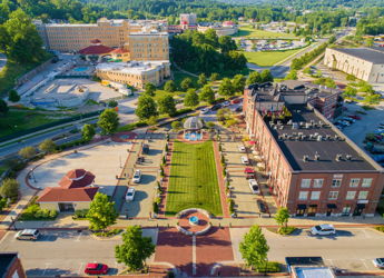 Aerial view of a vibrant town square with greenery, diverse buildings, and a central fountain, evoking community and tranquility.
